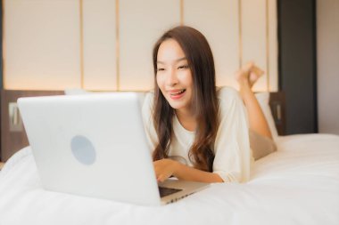Güzel bir Asyalı kadın yatak odasının içinde dizüstü bilgisayar kullanıyor.
