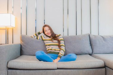 Güzel bir Asyalı kadın portresi. Oturma odasındaki kanepede rahatça gülümse.