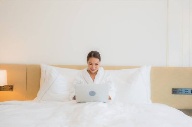 Güzel bir Asyalı kadın yatak odasının iç kısmında bilgisayar kullanıyor.