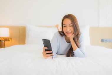 Güzel bir Asyalı kadın yatak odasının içinde akıllı cep telefonu kullanıyor.
