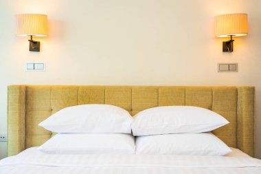 Yatak odasının içinde lamba süslemesi olan beyaz yastık ve battaniye.