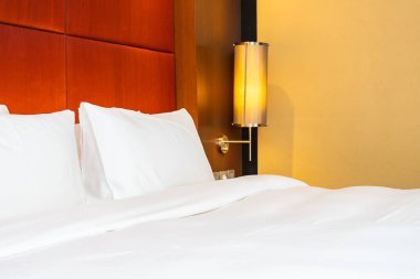 Beyaz yastık ve battaniye yatak odasının içinde lamba süslemesi olan yatakta.