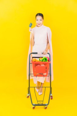 Sarı arka planda süpermarketten alınmış sepetli güzel Asyalı kadın portresi.