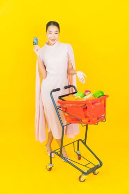 Sarı arka planda süpermarketten alınmış sepetli güzel Asyalı kadın portresi.