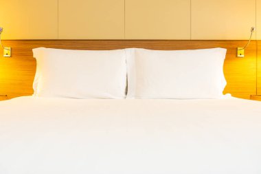 Yatak odasının içinde lamba süslemesi olan beyaz rahat yastık ve battaniye.