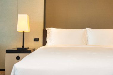 Yatak odasının içinde lamba süslemesi olan beyaz rahat yastık ve battaniye.