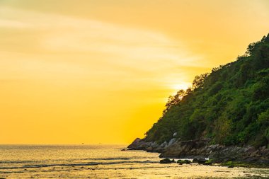 Sahildeki okyanusun etrafındaki dağda güzel bir gün batımı ve doğa gezisi için kaya.