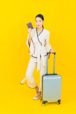 Güzel, genç, iş kadını, bavul ve pasaportlu Asyalı kadın, sarı arka planda seyahat etmeye hazır.