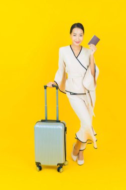 Güzel, genç, iş kadını, bavul ve pasaportlu Asyalı kadın, sarı arka planda seyahat etmeye hazır.