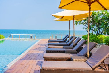 Otel tatil beldesinde açık havuz etrafında güzel boş sandalye şemsiyesi.