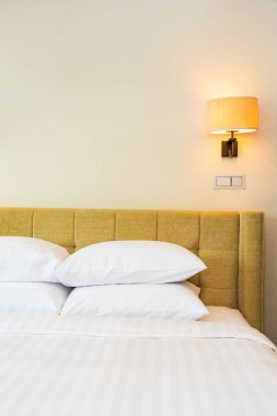 Yatak odasının içinde lamba süslemesi olan beyaz yastık ve battaniye.