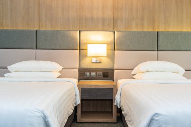 Yatak odasının içinde lamba süslemesi olan beyaz rahat yastık ve battaniye.