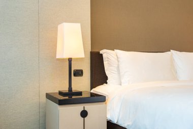 Yatak odasının içinde lamba süslemesi olan beyaz rahat yastık ve battaniye.