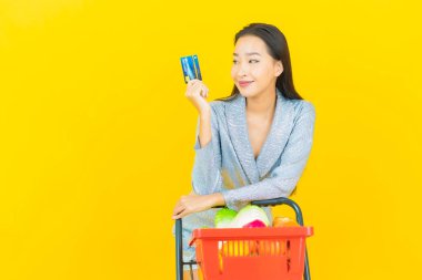 Asyalı güzel bir kadının portresi. Sarı arka planda süpermarketten alınmış alışveriş sepetiyle gülümsüyor.