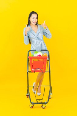 Asyalı güzel bir kadının portresi. Sarı arka planda süpermarketten alınmış alışveriş sepetiyle gülümsüyor.