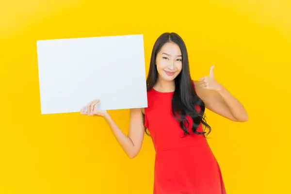 年轻美丽的亚洲女子面带微笑 黄色背景上贴着空白的白色广告牌 — 图库照片