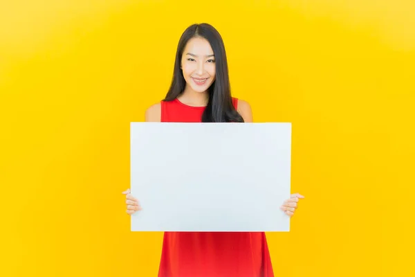 年轻美丽的亚洲女子面带微笑 黄色背景上贴着空白的白色广告牌 — 图库照片