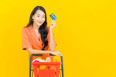 Asyalı güzel bir kadının portresi. Sarı arka planda süpermarketten alınmış alışveriş sepetiyle gülümsüyor.