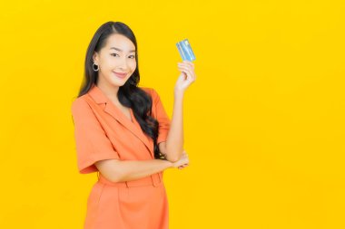 Asyalı güzel bir kadının portresi. Sarı arka planda kredi kartıyla gülümsüyor.