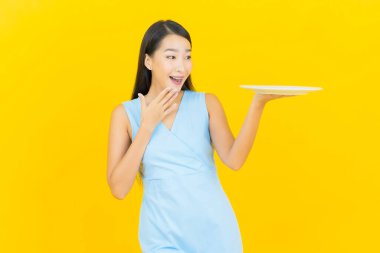 Asyalı güzel bir kadının portresi. Sarı arka planda boş tabak tabağıyla gülümsüyor.