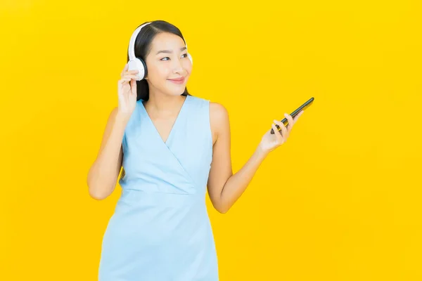 带着耳机和智能手机听黄色背景音乐的美丽年轻亚洲女人的画像 — 图库照片