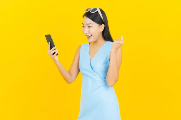 ポートレート美しいです若いですアジアの女性笑顔とともにスマートフォン上の黄色の色の背景 — ストック写真