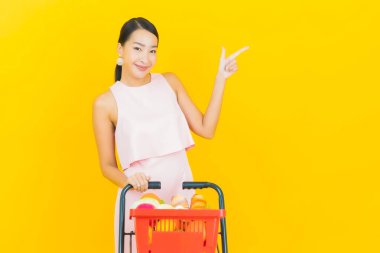 Asyalı güzel bir kadının portresi. Sarı arka planda süpermarketten alınmış alışveriş sepetiyle gülümsüyor.