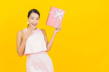 Asyalı güzel bir kadının portresi. Sarı arka planda kırmızı hediye kutusuyla gülümsüyor.