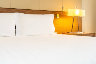 Yatak odasının içinde lamba süslemesi olan beyaz rahat yastık ve battaniye.