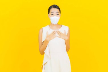 Sarı arka planda Covid19 veya virüsü korumak için maskeli güzel Asyalı kadın portresi