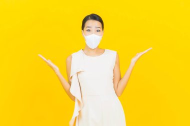 Sarı arka planda Covid19 veya virüsü korumak için maskeli güzel Asyalı kadın portresi