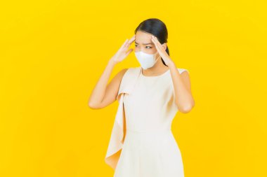 Sarı arka planda Covid19 veya virüsü korumak için maskeli güzel Asyalı kadın portresi