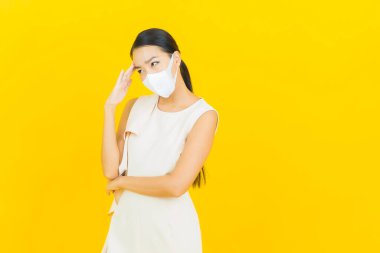 Sarı arka planda Covid19 veya virüsü korumak için maskeli güzel Asyalı kadın portresi