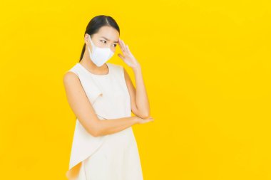 Sarı arka planda Covid19 veya virüsü korumak için maskeli güzel Asyalı kadın portresi