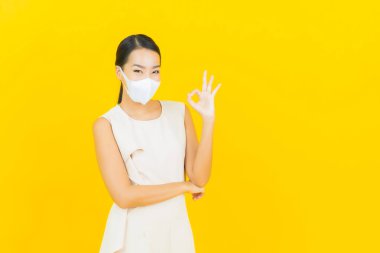 Sarı arka planda Covid19 veya virüsü korumak için maskeli güzel Asyalı kadın portresi