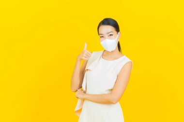 Sarı arka planda Covid19 veya virüsü korumak için maskeli güzel Asyalı kadın portresi