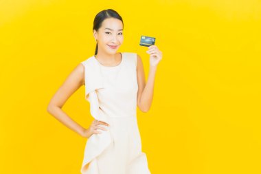 Asyalı güzel bir kadının portresi. Sarı arka planda kredi kartıyla gülümsüyor.