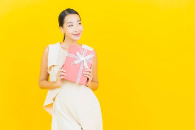 Asyalı güzel bir kadının portresi. Sarı arka planda kırmızı hediye kutusuyla gülümsüyor.