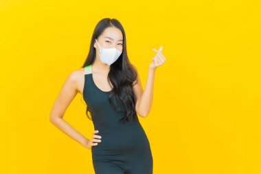 Güzel bir Asyalı kadın, sarı arka planda egzersiz için spor kıyafeti giyer.