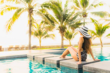 Güzel bir Asyalı kadın portresi, gün batımında palmiye ağacıyla birlikte havuz kenarında dinleniyor ya da tatil için gün doğumunda dinleniyor.