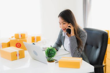 Güzel Asyalı iş kadını portresi evden bilgisayarlı cep telefonuyla karton kutuyla çevrimiçi alışveriş için hazır bekliyor.