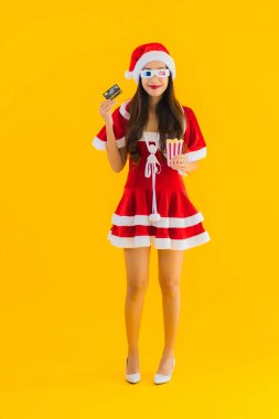 Güzel bir Asyalı kadın portresi patlamış mısır ve 3D gözlüklü noel şapkası takıyor sarı izole edilmiş arka planda film izlemeye hazır.