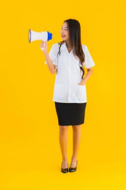 Güzel bir Asyalı genç doktor portresi. Sarı izole arka planda megafon kullanıyor.