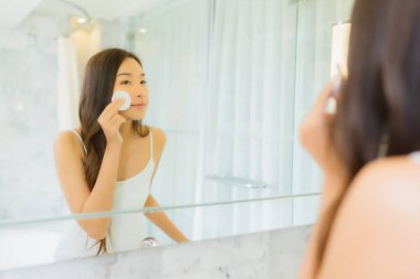 Güzel bir Asyalı kadın portresi. Banyo içerisindeki aynada yüzünü kontrol et ve makyaj yap.