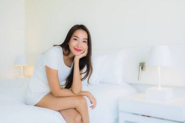 Güzel bir portre genç Asyalı kadın rahatla. Yatak odasının iç tarafında beyaz yastık battaniyesiyle mutlu bir gülümseme.