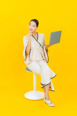 Sarı arka planda bilgisayar bilgisayarı olan güzel bir iş kadını portresi.