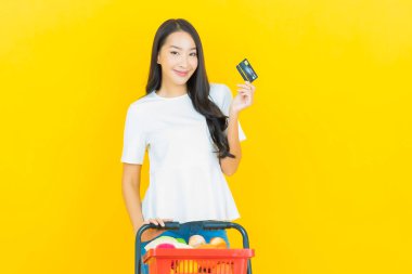 Asyalı güzel bir kadının portresi. Sarı arka planda süpermarketten alınmış alışveriş sepetiyle gülümsüyor.