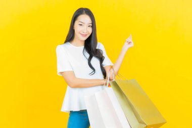 Sarı arka planda alışveriş çantasıyla gülümseyen güzel Asyalı kadın portresi