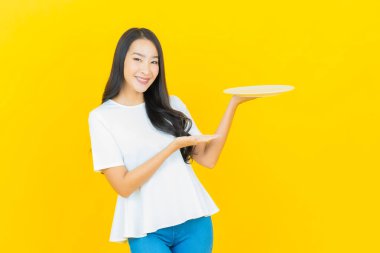 Asyalı güzel bir kadının portresi. Sarı arka planda boş tabak tabağıyla gülümsüyor.