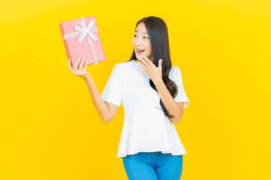 Asyalı güzel bir kadının portresi. Sarı arka planda kırmızı hediye kutusuyla gülümsüyor.